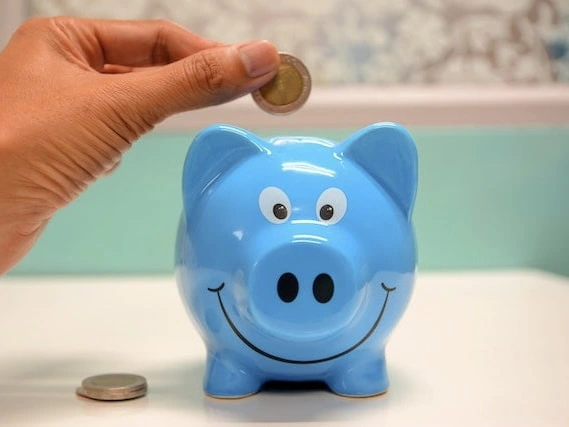Someone is putting a coin into a blue piggy bank.