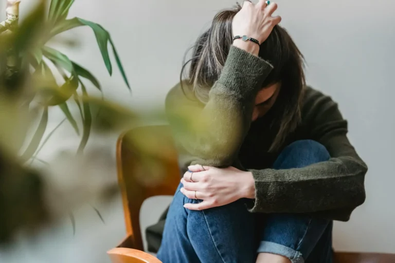 A woman sits on the floor holding her head in her hand.